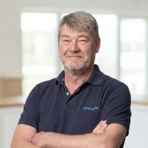 VIMAB-medarbetare med korslagda armar och VIMAB-logotyp på pikétröja, ler mot kameran