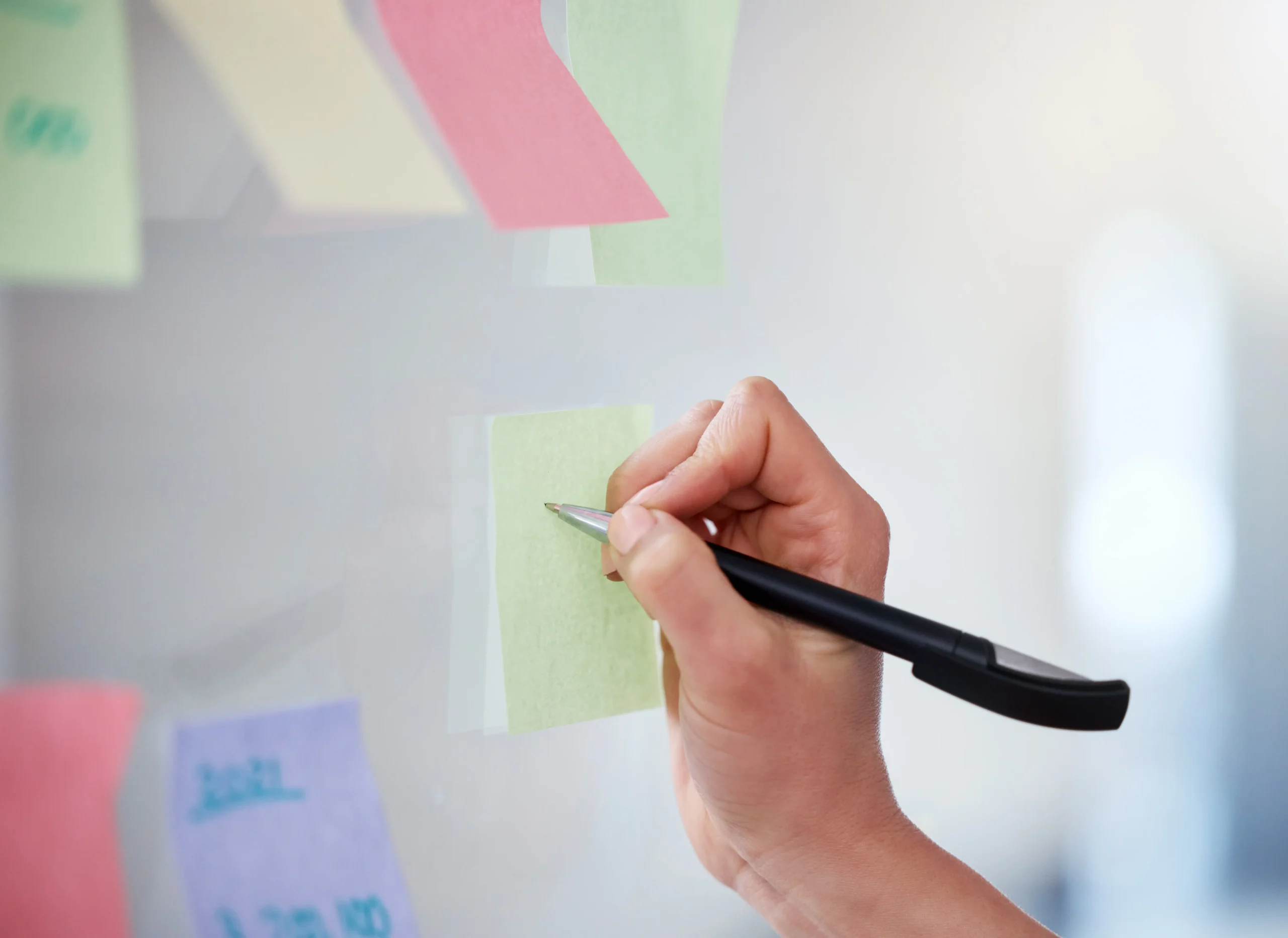 Hand skriver på grön post-it-lapp på glasvägg täckt med färgglada anteckningar – planering av ventilservice